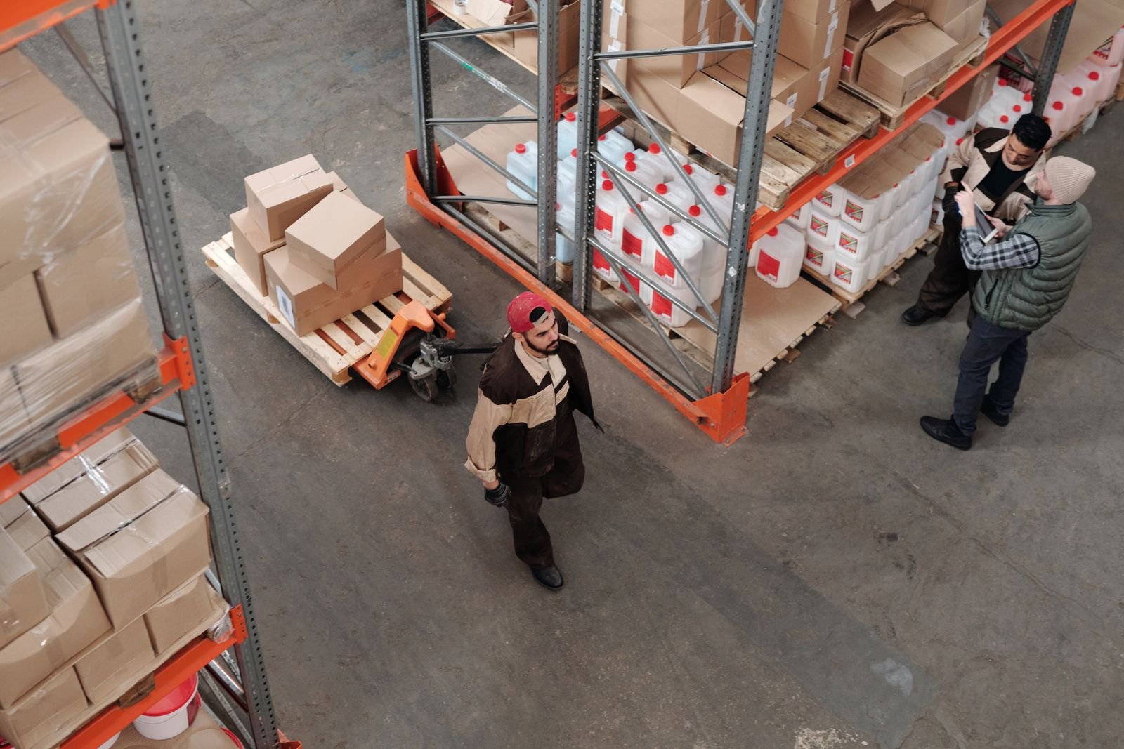 Workers moving pallets inside a racked industrial warehouse