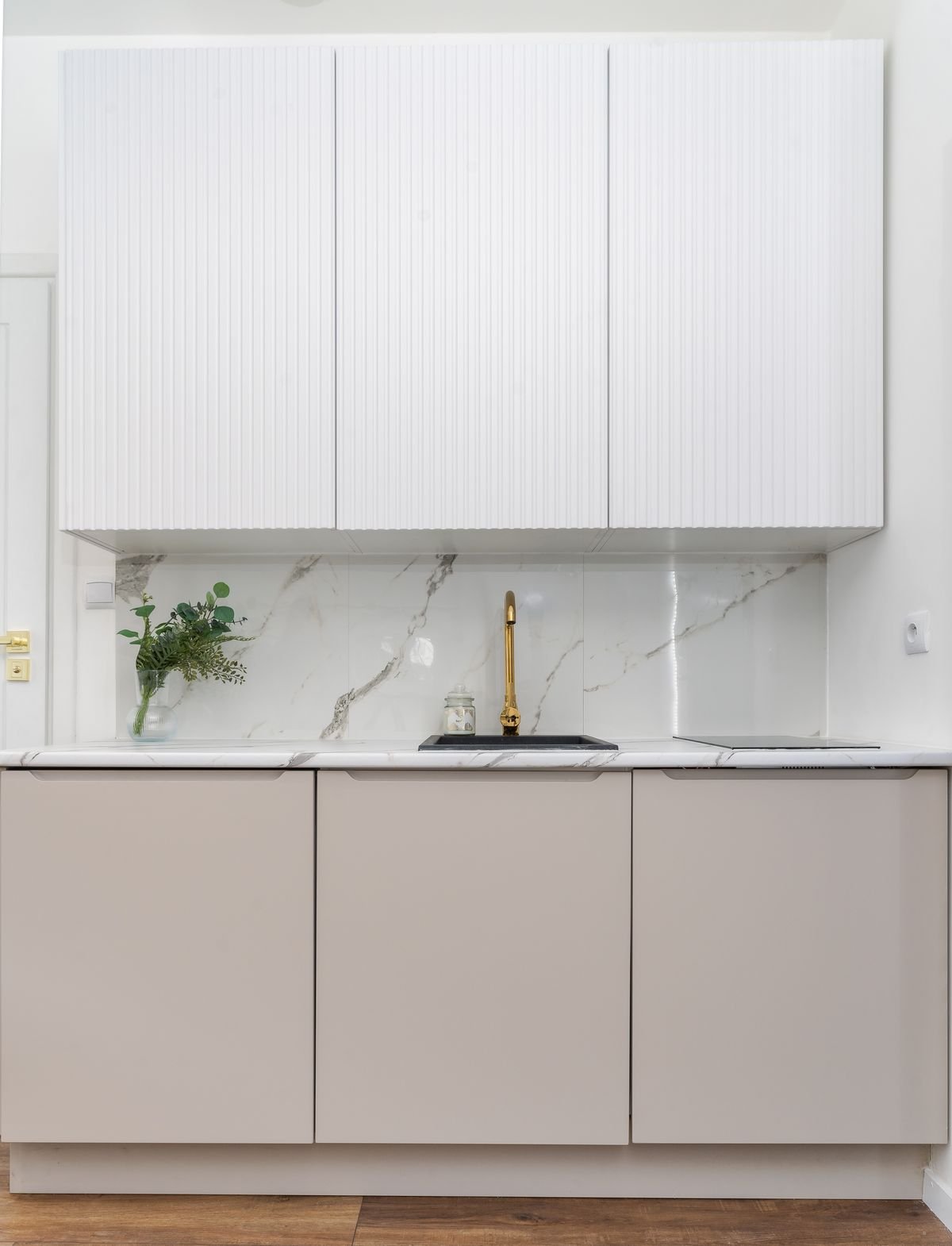 Luxurious minimalist kitchen with marble backsplash and a gold faucet, staged for sale