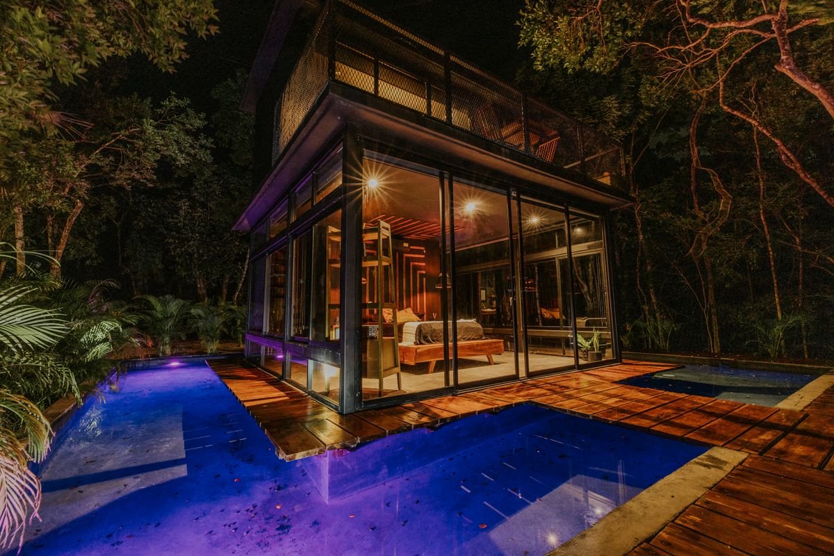 Glass-walled Los Angeles home glowing beside its private pool at night