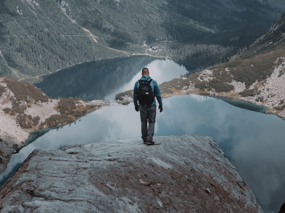 A hiker standing at the edge of a mountain lake with a pack on