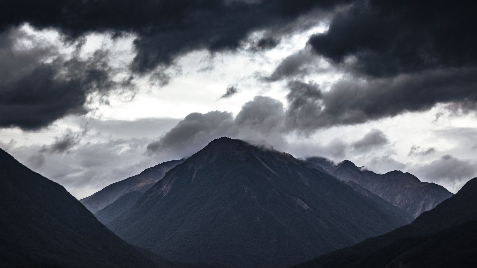 A wide range of dark mountains under low cloud
