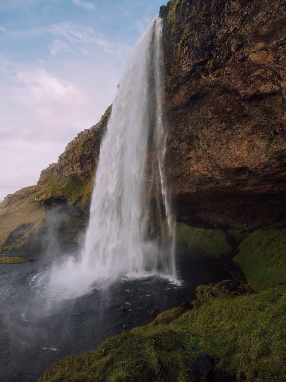 A wide Icelandic waterfall falling over dark basalt rock into a river