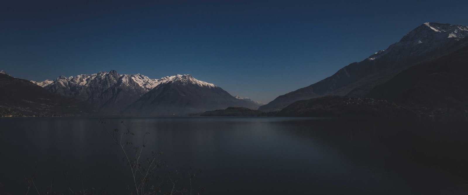 A still mountain lake at blue hour with a single figure sitting on the rocks near the water