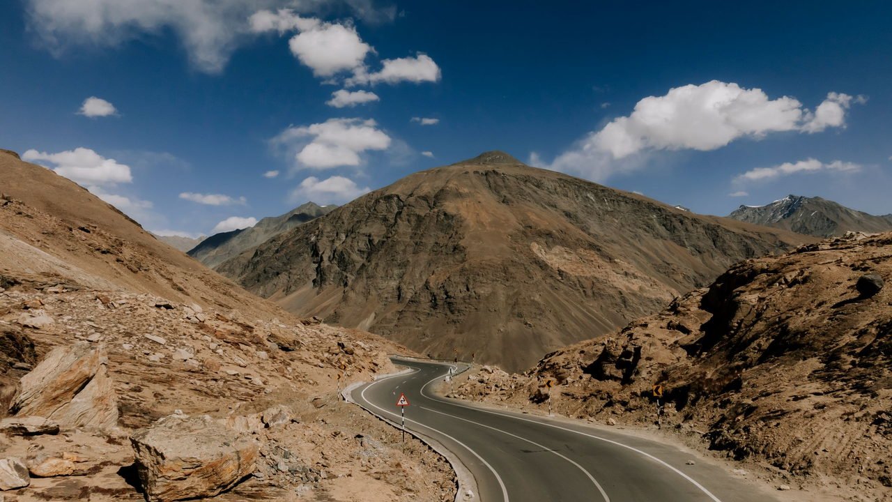 An empty high-altitude road running through the bare brown mountains of Ladakh