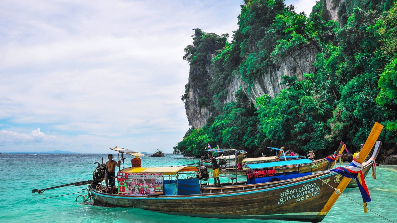 Limestone karsts rising out of turquoise water in Thailand with a longtail boat below them