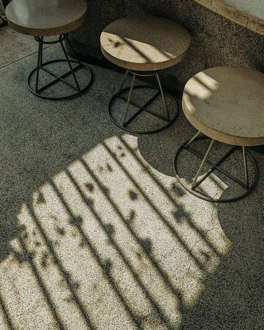 Afternoon light through a screen throwing a striped shadow across a terrazzo floor and three round stools