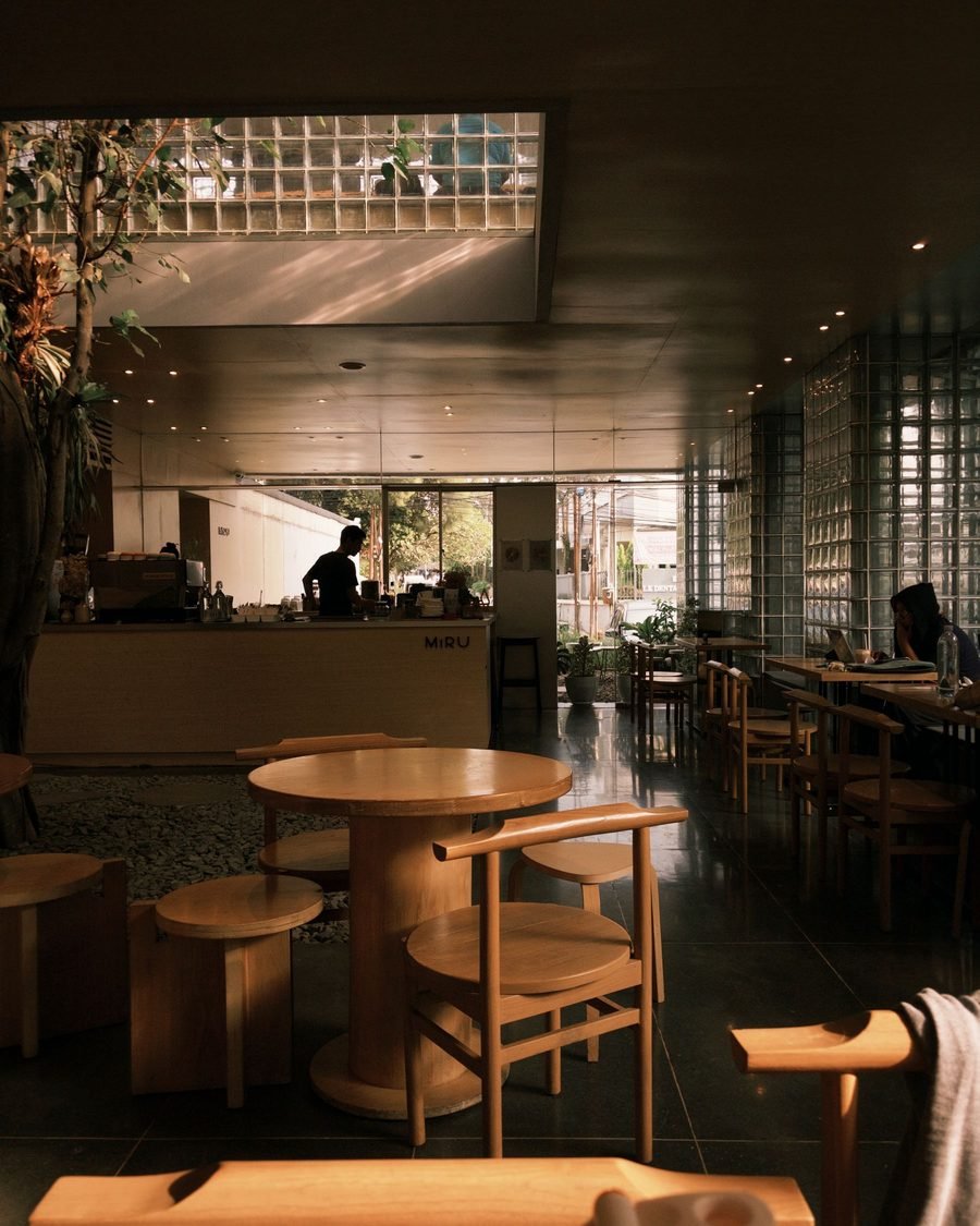 Cafe interior with a glass-block clerestory, timber counter and round timber tables under warm daylight