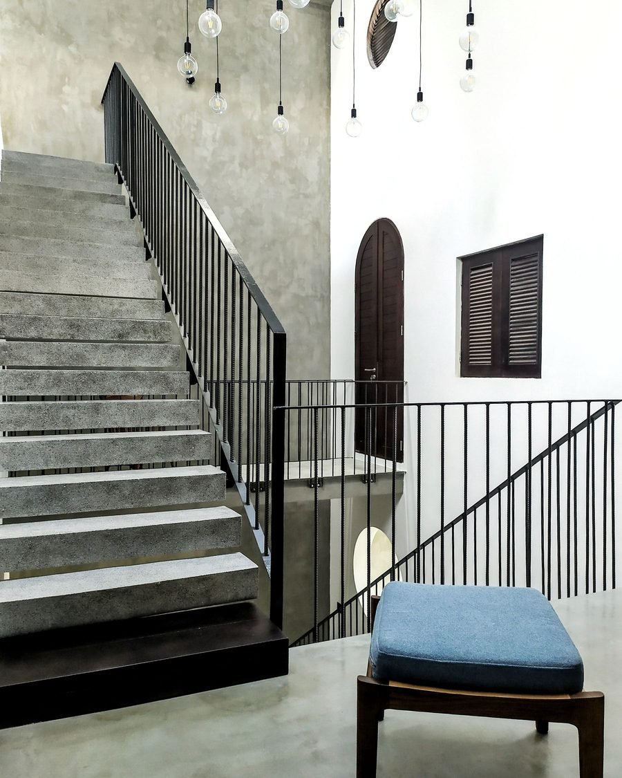 In-situ concrete staircase with a slim black steel balustrade rising past an arched opening in a white wall