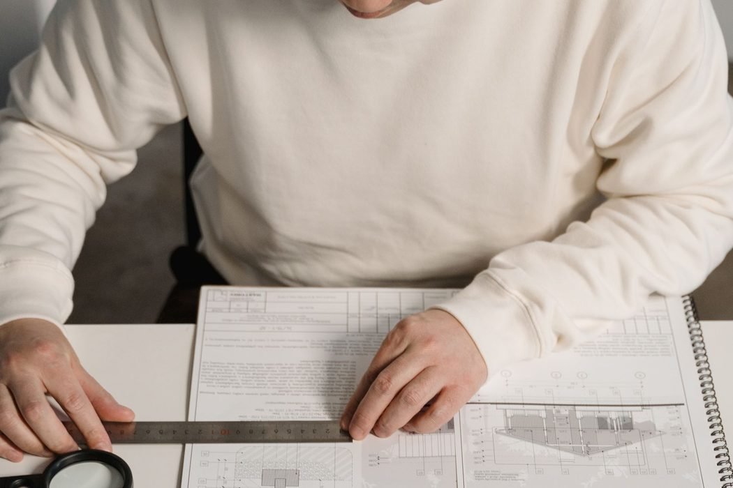 Overhead view of an architect working over a dimensioned drawing with a scale rule and card model pieces