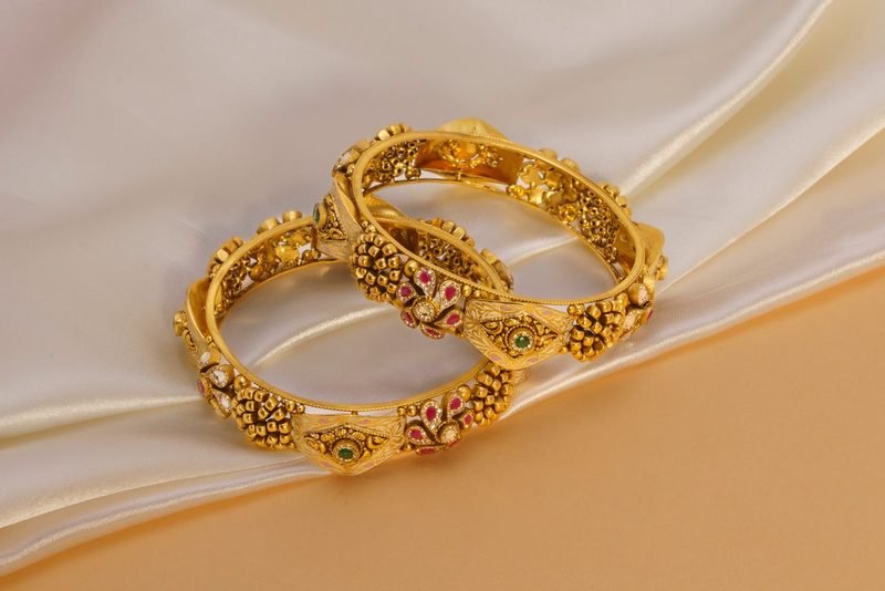 A pair of ornate gold bangles set with pear-cut stones on a dark background