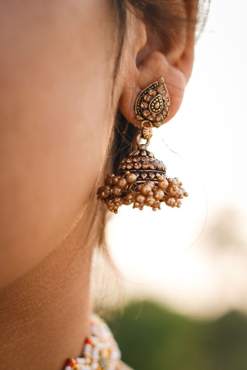 An antique-finish gold jhumka earring with a pearl fringe worn against the light