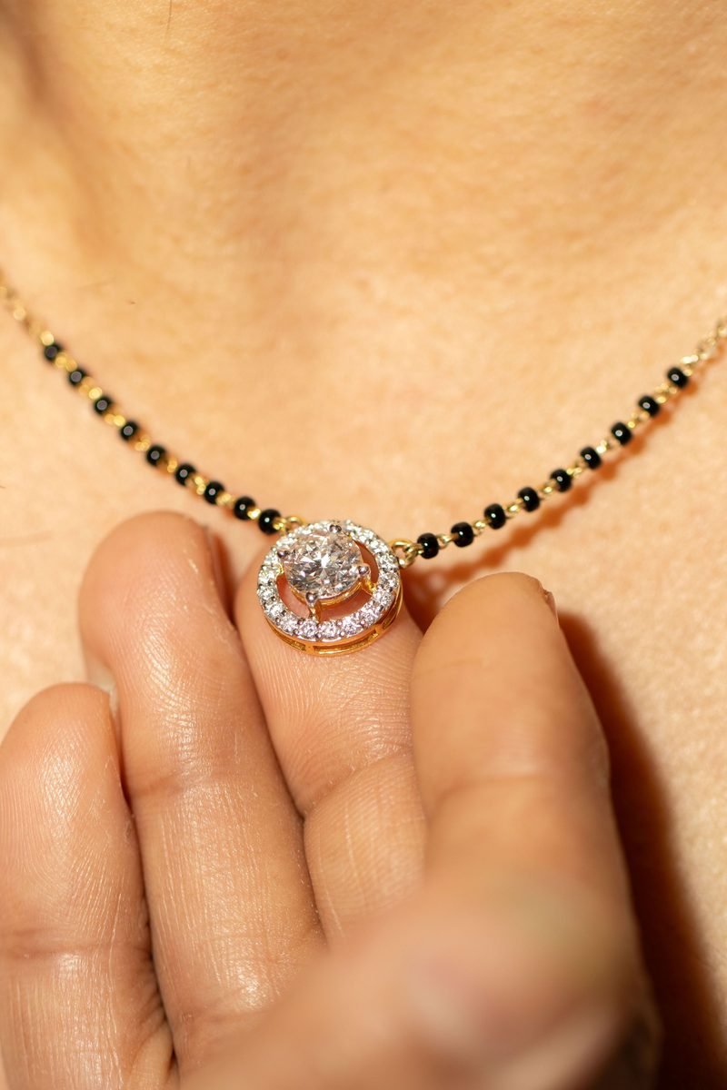 A gold chain with a starburst pendant set with a round solitaire, laid on white silk