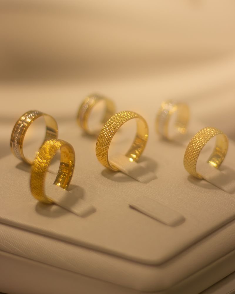 Six textured 22-karat gold bands standing on a cream jewellery display tray
