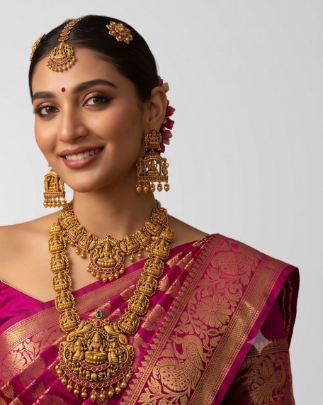 A bride in a magenta Kanjeevaram silk saree wearing a traditional Lakshmi temple gold haram, choker, and temple jhumkas