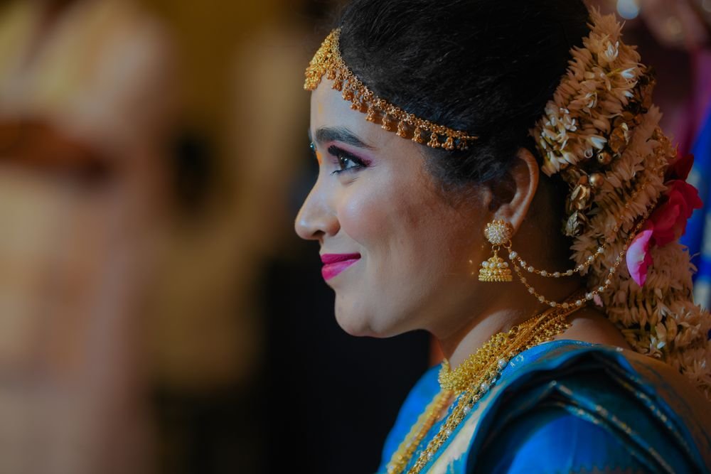 Profile of a woman in a blue silk saree wearing a temple gold jhumka with an ear chain and a long chain