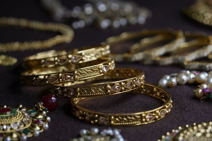 Four antique-finish gold bangles set with pear-cut stones laid on a dark velvet tray with pearl strands behind