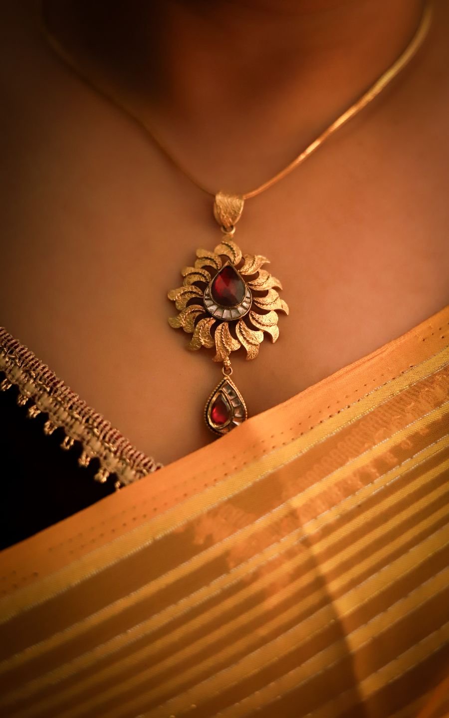 A sunflower-shaped antique gold pendant with a pear-cut ruby centre and a polki drop, worn over a yellow silk saree