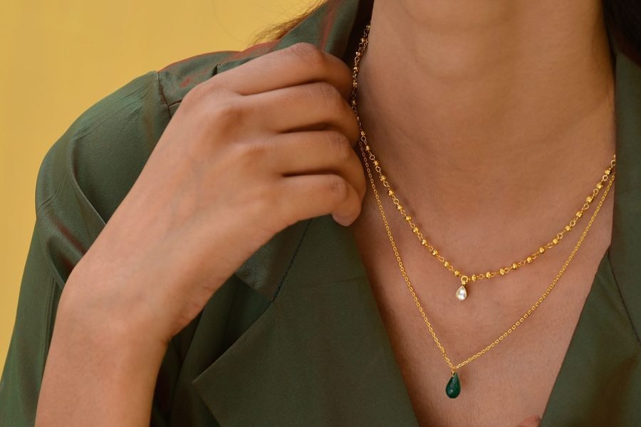 Two layered gold chains with coin pendants worn over a plain beige t-shirt
