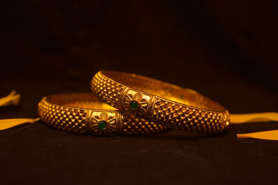 A pair of heavy textured 22-karat gold bangles with green cabochon emeralds set into a floral boss