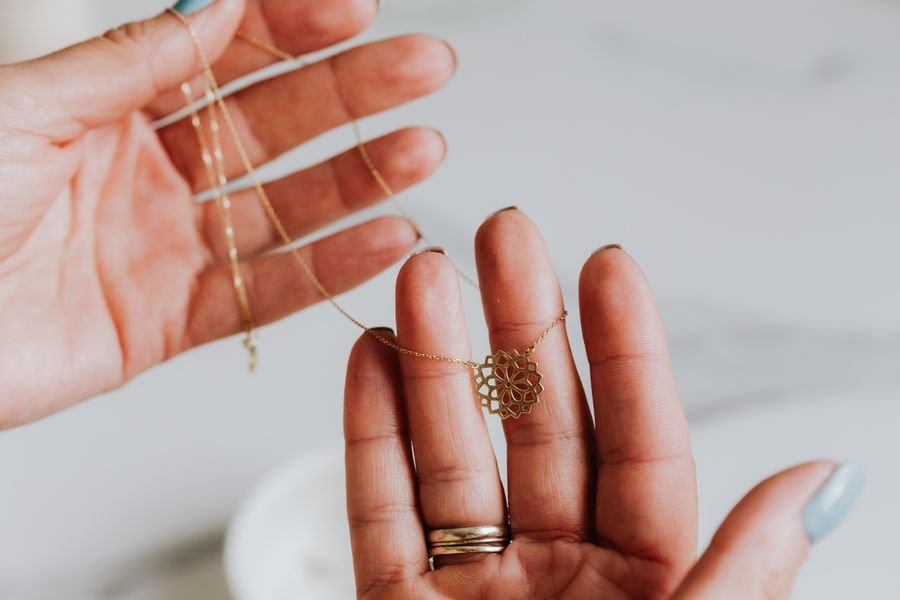 A fine gold chain with a cut-work lotus pendant held across an open palm