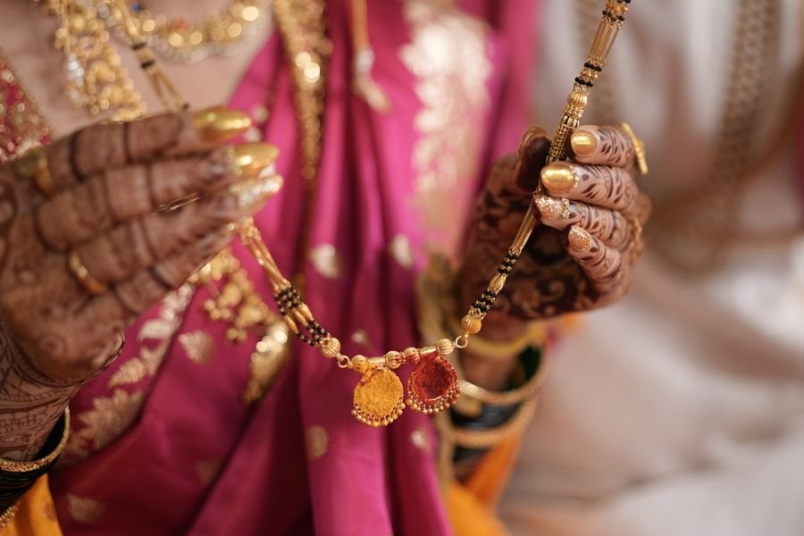 Hennaed hands holding a short gold mangalsutra strung with black beads and two enamelled vati pendants
