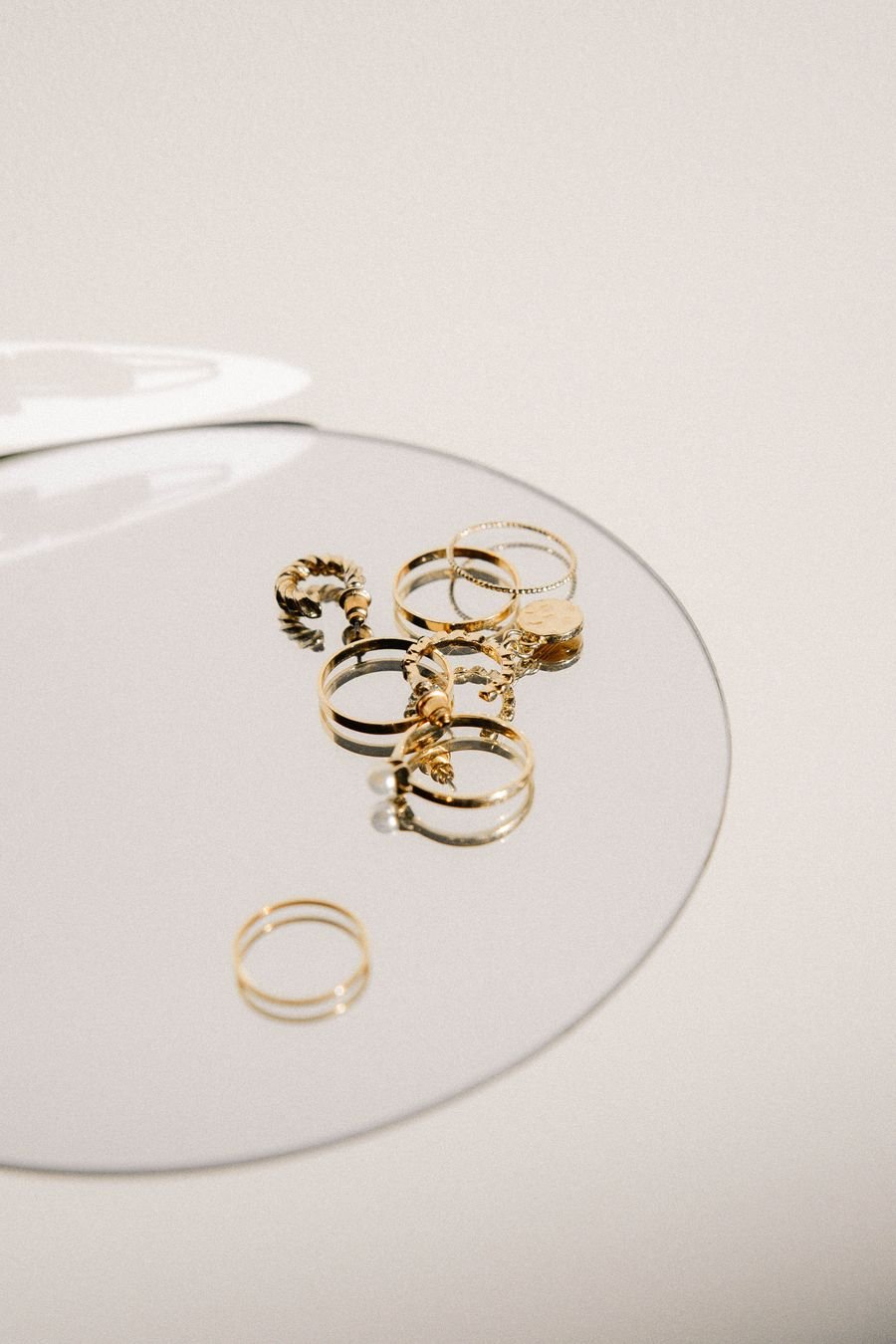 Five slim gold stacking rings arranged on a round mirror against a cream background