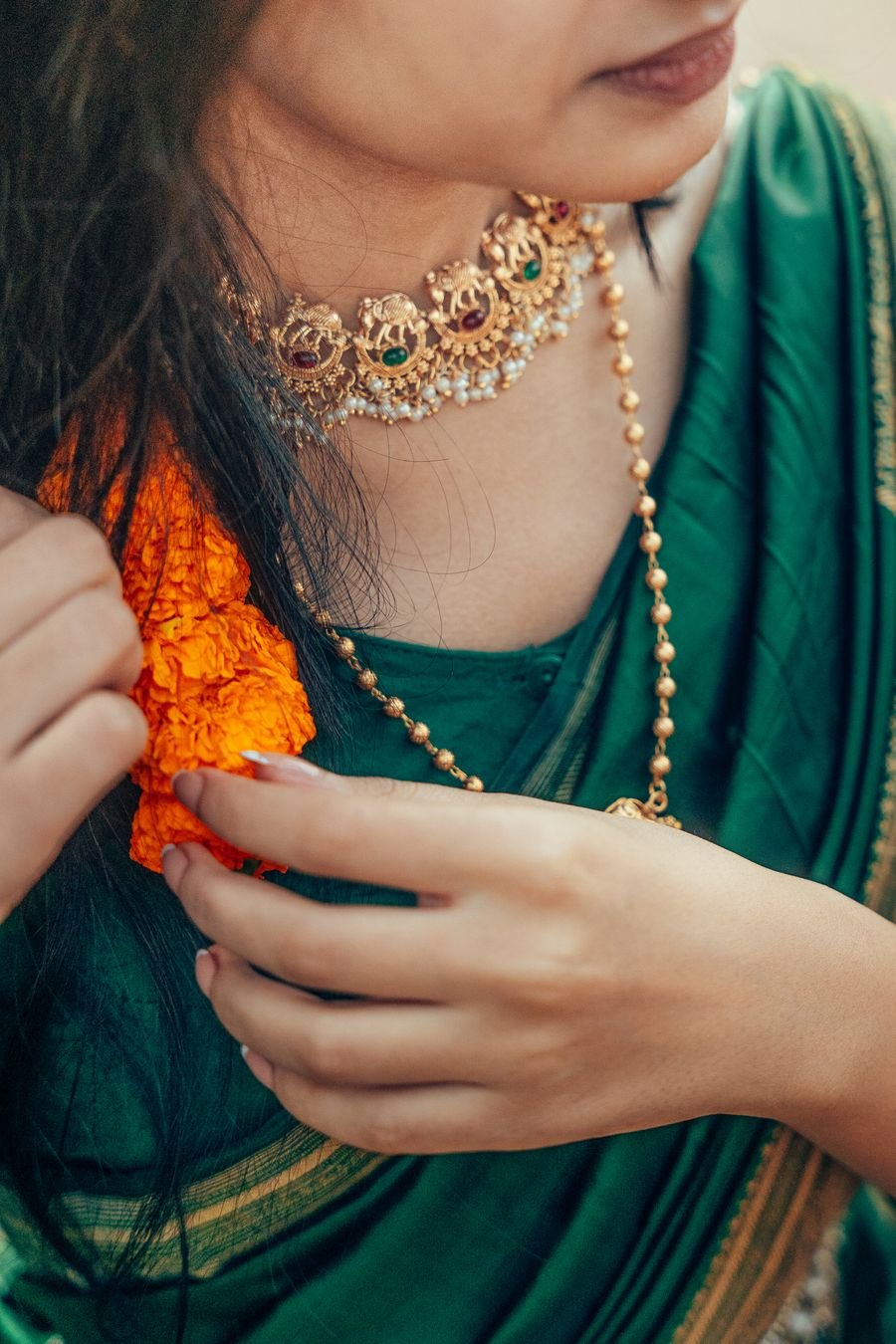 A temple gold choker with elephant motifs, emerald and ruby stones and a pearl fringe, worn over a green silk saree