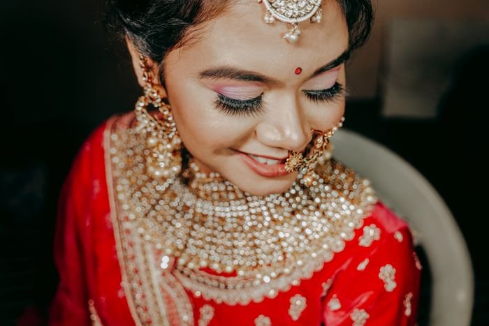 A bride in a red outfit wearing layered pearl and gold necklaces