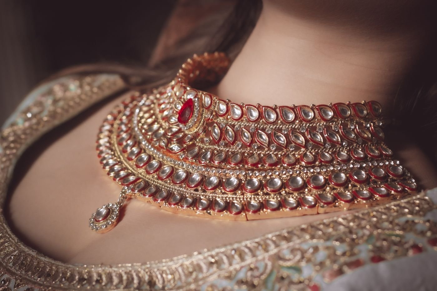 A bride wearing a wide kundan choker with red enamel and uncut stones over gold-embroidered dupatta