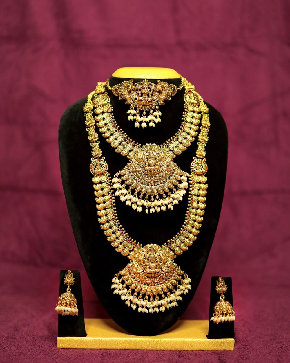 Antique-finish gold temple jewellery set — choker, long haram and jhumka earrings displayed on black velvet bust