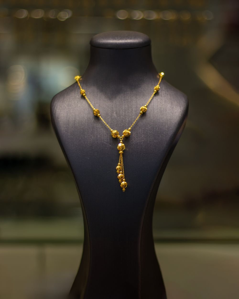 A light gold chain with beaded stations and tassel drop on display bust in showroom