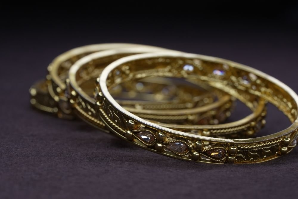 Four ornate gold bangles with pear-cut stones stacked on dark surface