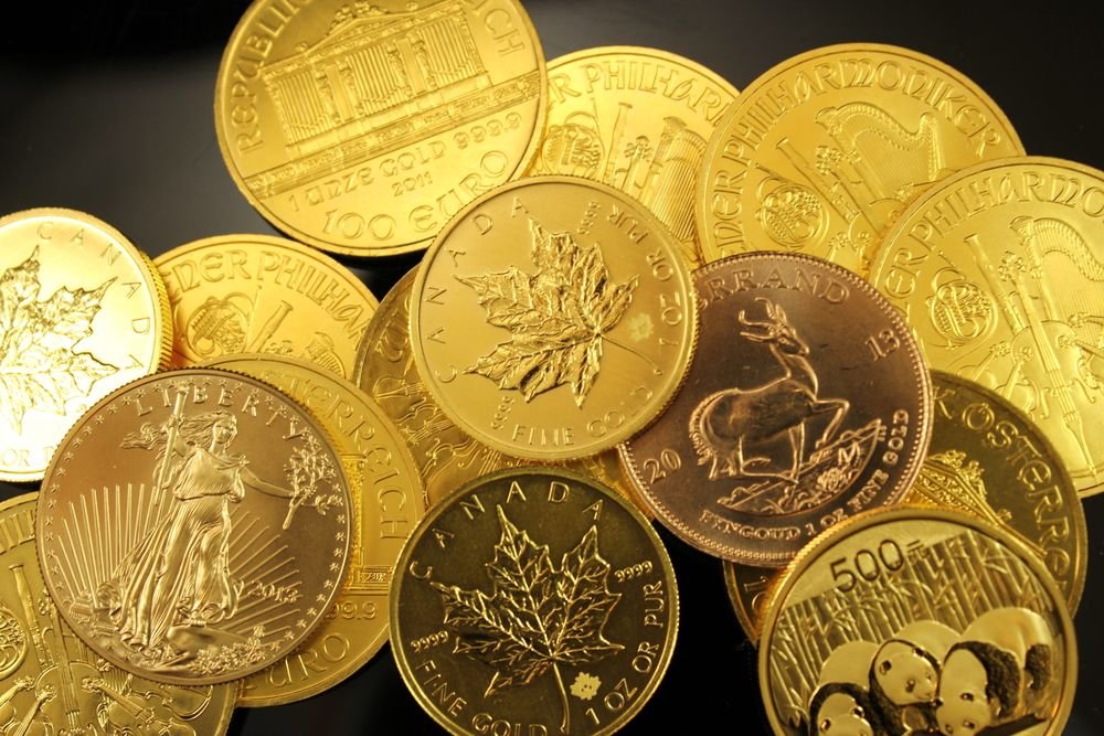 Assorted 24-karat gold bullion coins arranged on dark reflective surface