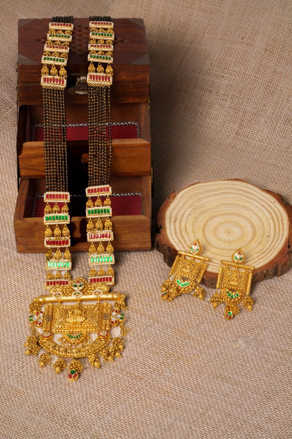Long gold mangalsutra with black beads and a Lakshmi pendant, with matching earrings, on jute cloth