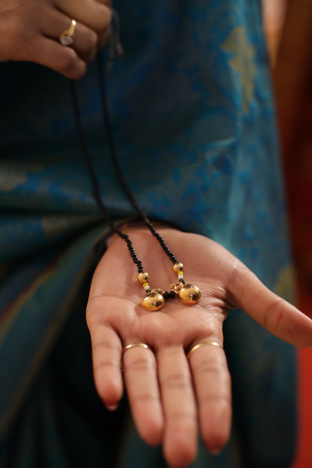 A woman holding a gold two-vati mangalsutra with black beads in her open palm