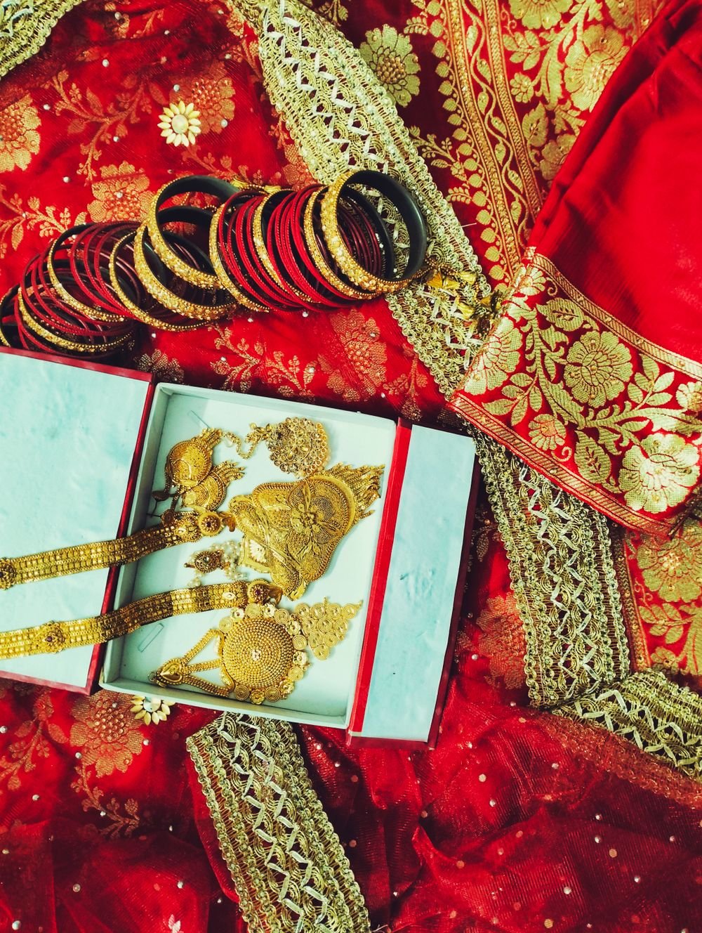 Family gold chains, haar, and bangles in open box on red saree for counter purity testing